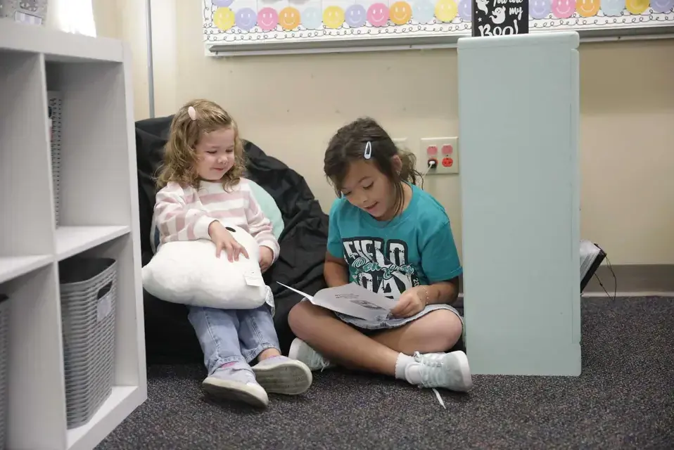 Early Childhood and Lower School students reading together and smiling