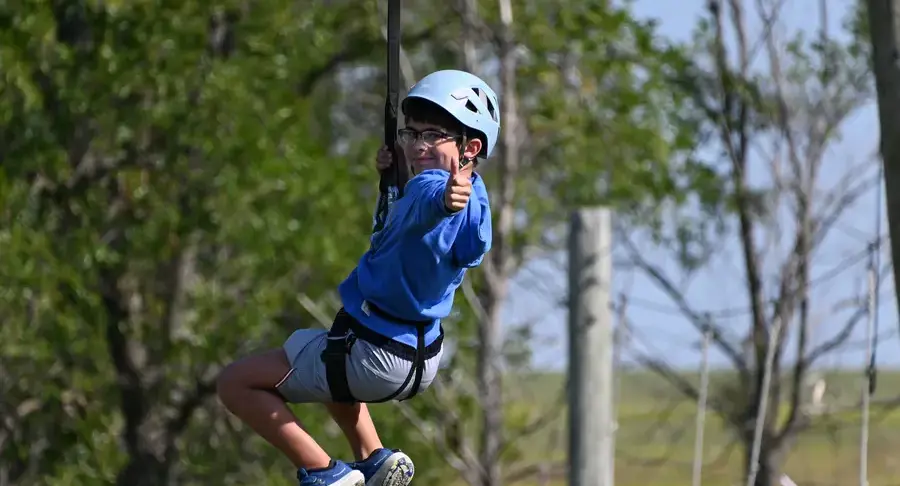 Middle school students gives a thumbs up while ziplining during a school trip
